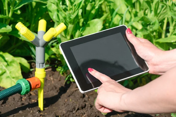 Person steuert mit einem Tablet die Bewässerung im Garten.